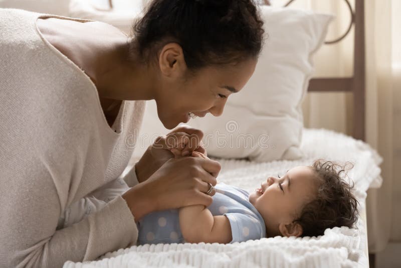 Sleende afrikansk amerikansk mor leker med liten dotter i sovrummet