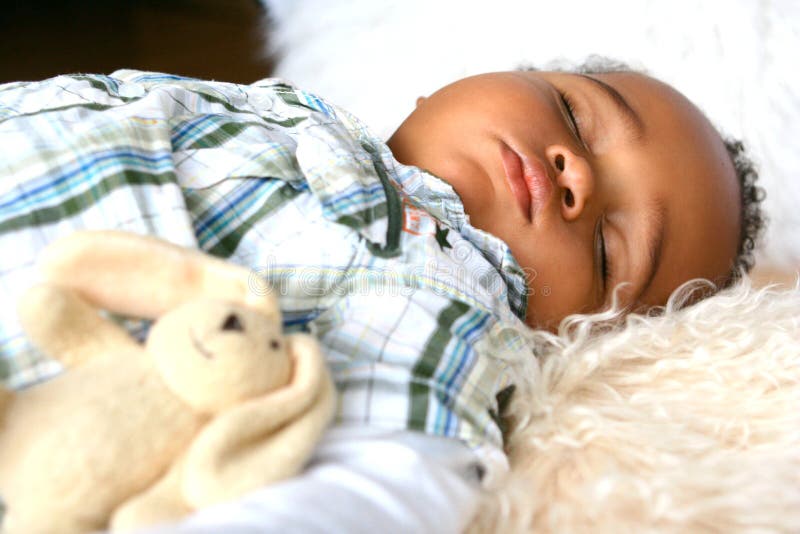 Beautiful toddler of mix parentage sleeping peacefully on sheepskin rug accompanied by his fluffy bunny toy. Beautiful toddler of mix parentage sleeping peacefully on sheepskin rug accompanied by his fluffy bunny toy.
