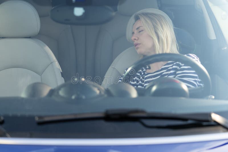 Sleeping in car: female driver tired of driving long road has nap on front seat on parking stop