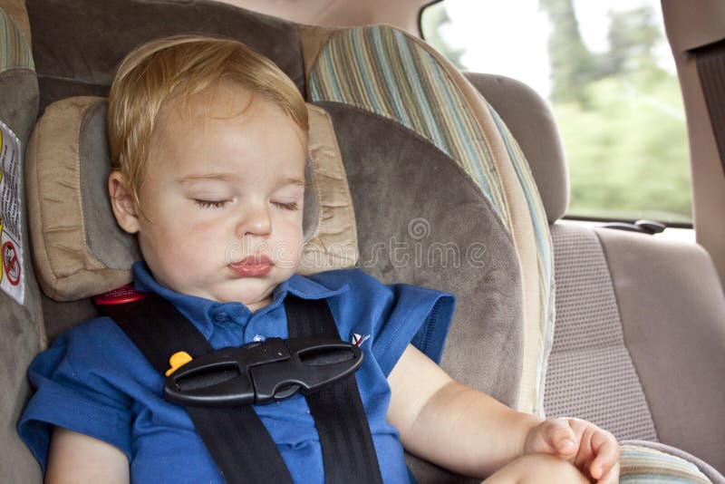 A one year old, blonde haired baby boy in a blue shirt, sitting in a buckled car seat in the back of a vehicle, sound asleep with his eyes closed. A one year old, blonde haired baby boy in a blue shirt, sitting in a buckled car seat in the back of a vehicle, sound asleep with his eyes closed