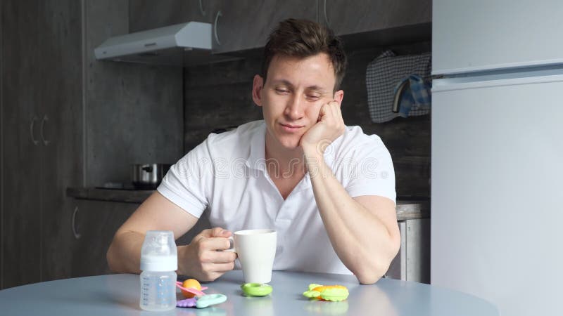 Sleepy father naps and drinks cup of coffee in kitchen