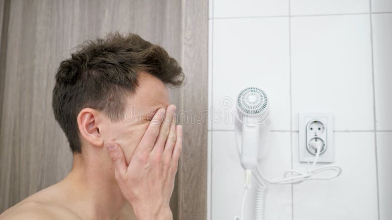 Sleepy man stands in bathroom opening and closing eyes