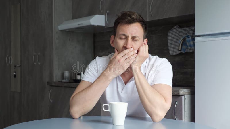 Sleepy man yawns and wants to sleep over cup of coffee