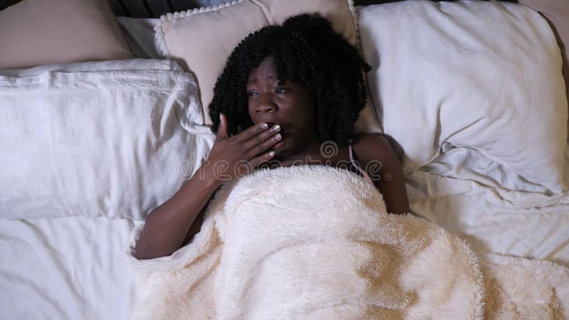 Sleepy young black woman yawns lying on queen-size bed slow