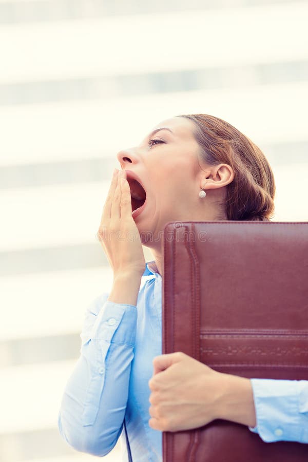 Its is too early for this meeting. Closeup portrait sleepy young business woman, running to work wide open mouth yawning, eyes closed looking bored isolated outside corporate office windows background