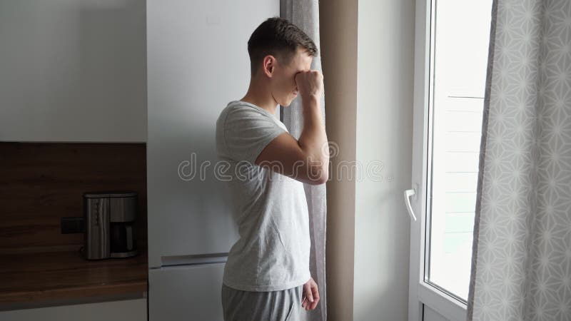 Sleepy young man comes up yawning to the window in the kitchen