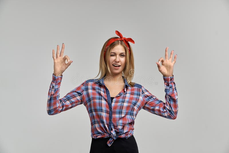 Slender attractive young blonde woman winks and shows OK sign. Studio portrait on isolated background royalty free stock photography Slender attractive young blonde woman winks and shows OK sign. Studio portrait on isolated background royalty free stock photography