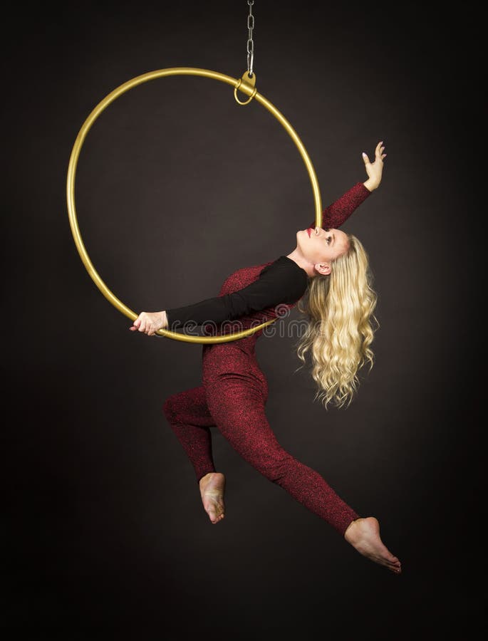 A slender blonde girl-an air acrobat in a red suit with long hair , performs exercises in an air ring
