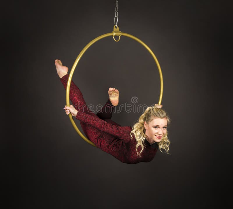 A slender blonde girl-an air acrobat in a red suit with long hair , performs exercises in an air ring