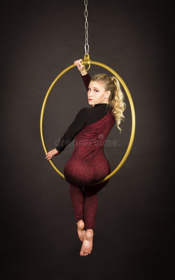 A slender blonde girl-an air acrobat in a red suit with long hair , performs exercises in an air ring