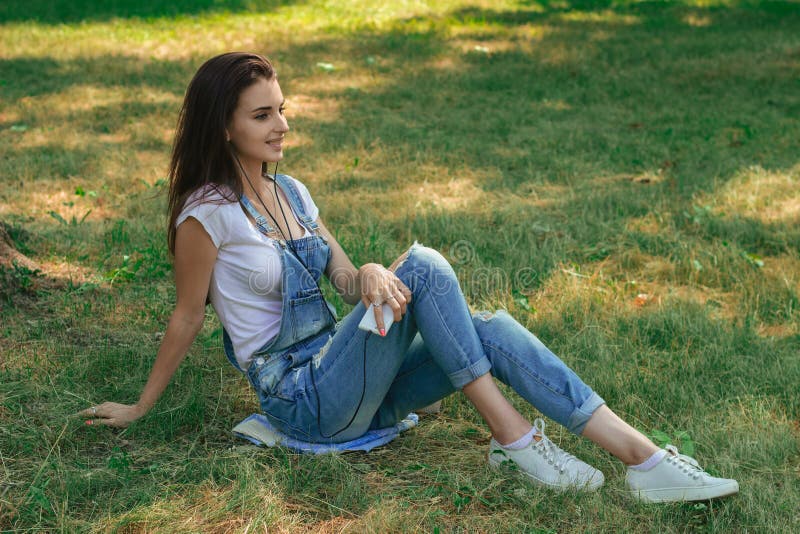 Slender Brunette Teen in Jeans Overalls Lying on the Grass in the Park ...