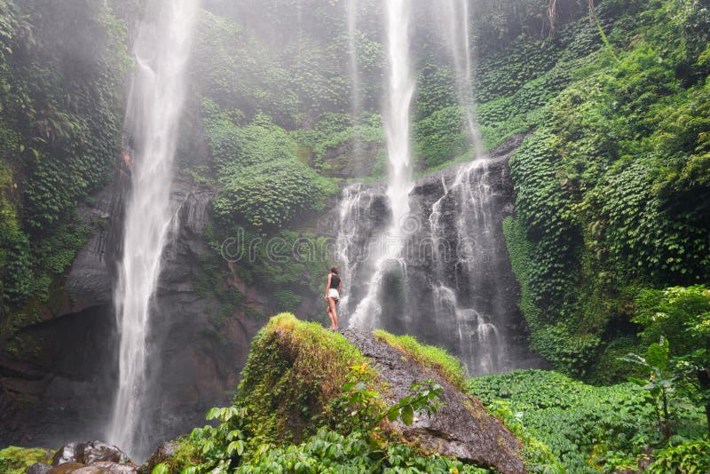 Slender girl standing in front of a waterfall on a rock royalty free stock photos Slender girl standing in front of a waterfall on a rock royalty free stock photos