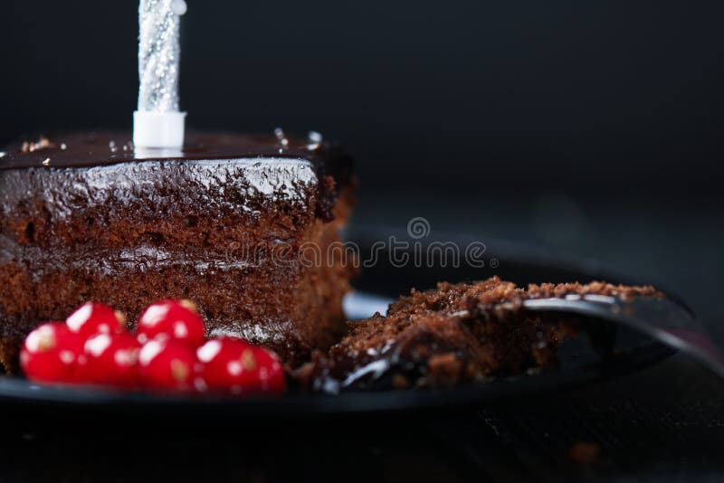 Slice of chocolate cake with a single lit candle.