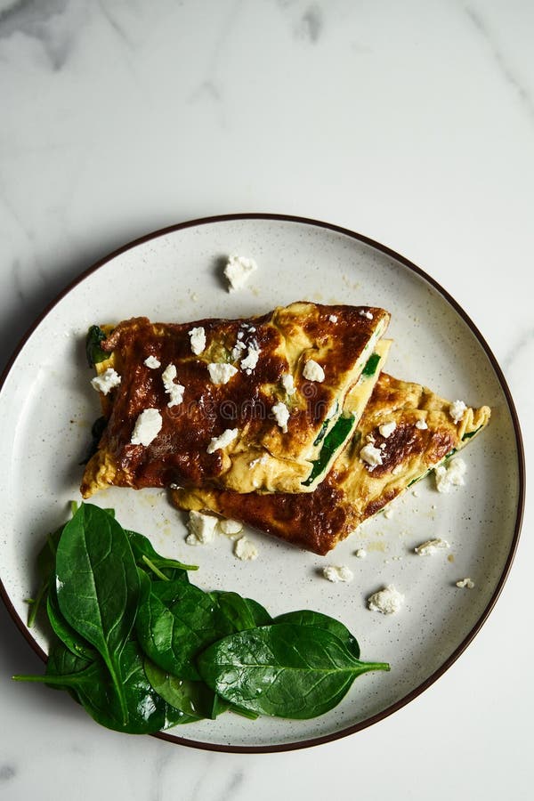 Sliced folded omelette stuffed with spinach and feta on the white plate with spinach leaves on back. Healthy and dietary royalty free stock photography Sliced folded omelette stuffed with spinach and feta on the white plate with spinach leaves on back. Healthy and dietary royalty free stock photography