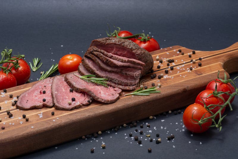 Sliced Grass Fed juicy Corn Roast Beef garnished with Tomatoes, Fresh Rosemary Herb and Rainbow Peppercorns