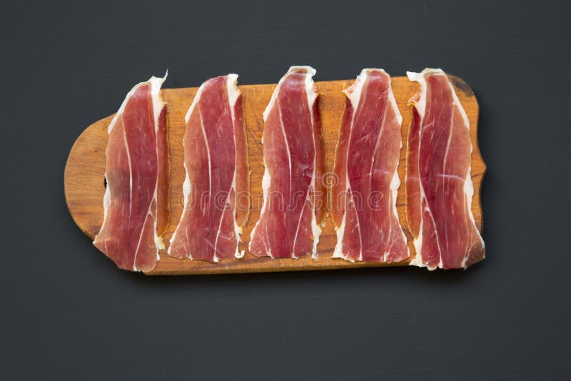 Sliced jamon Serrano or Iberico on cutting wooden board. Traditional spanish hamon on dark wooden background, top view. stock photography Sliced jamon Serrano or Iberico on cutting wooden board. Traditional spanish hamon on dark wooden background, top view. stock photography