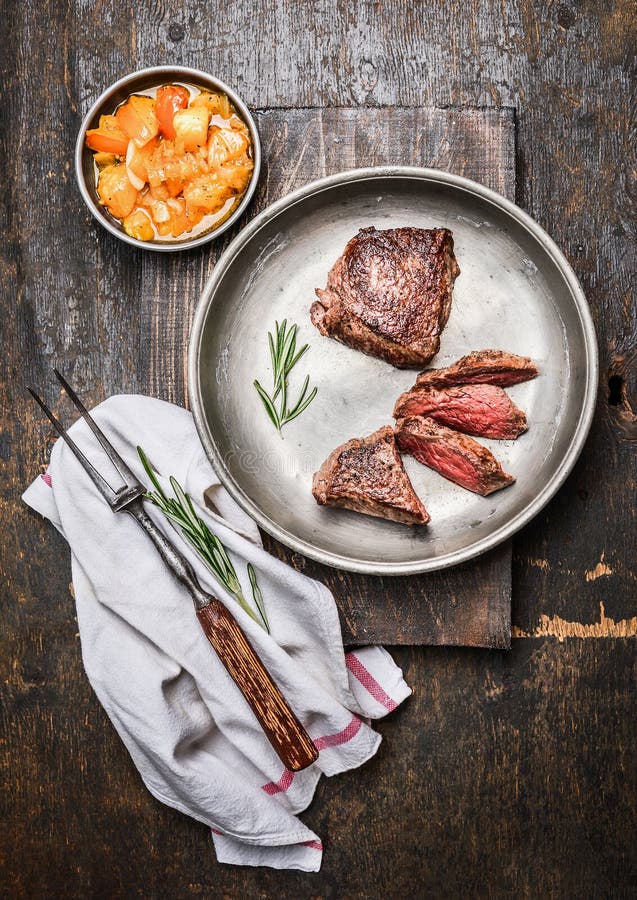 Sliced medium rare roasted beef steak, filet mignon , in metal rustic plate with meat fork and salsa sauce on dark wooden backgrou royalty free stock image Sliced medium rare roasted beef steak, filet mignon , in metal rustic plate with meat fork and salsa sauce on dark wooden backgrou royalty free stock image