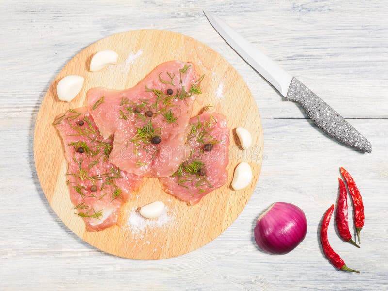 Sliced pieces of meat turkey game filet, fennel, garlic, allspice, red chili pepper on wooden cutting board, red onion, knife on