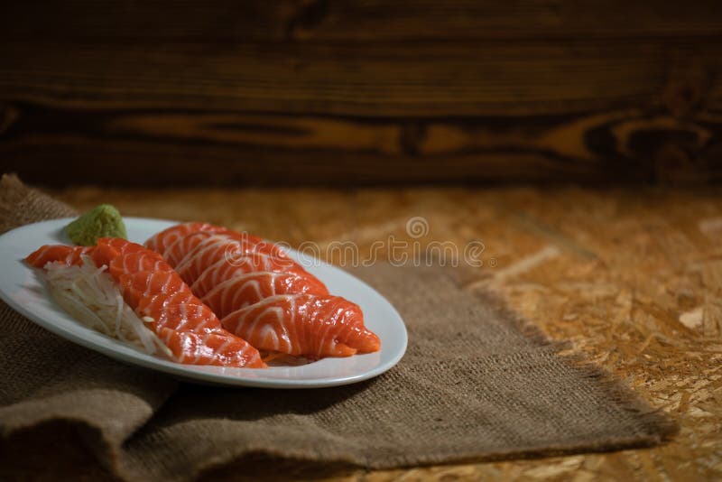 Sliced salmon placing on dish together wasabi and radish on wooden plate