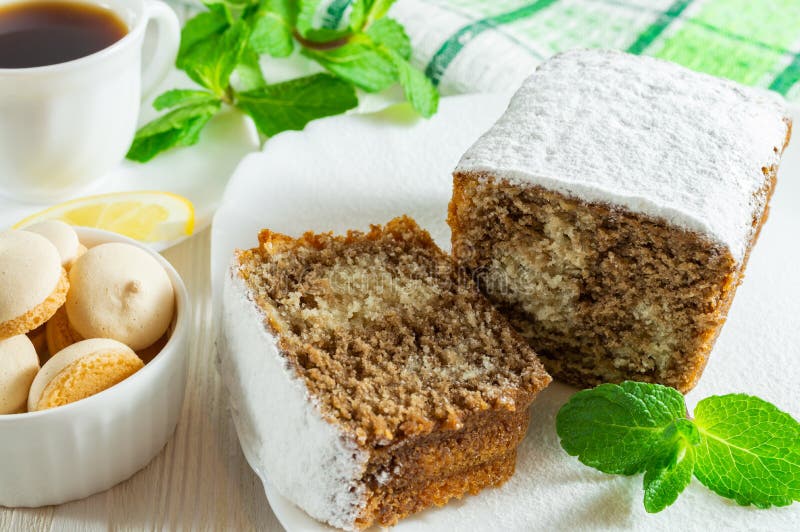 Slices of biscuit cake, a сup of tea with lemon, small cookies and mint leaves on a white wooden table. A few slices of biscuit cake with powdered sugar, a сup royalty free stock image Slices of biscuit cake, a сup of tea with lemon, small cookies and mint leaves on a white wooden table. A few slices of biscuit cake with powdered sugar, a сup royalty free stock image