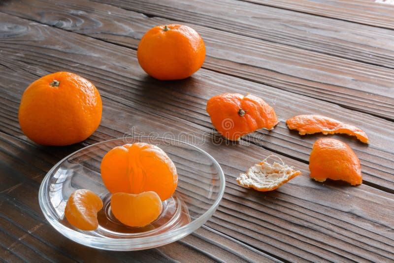 slices of orange and a ripe tangerine in glass saucer. Against the background the old wooden table.