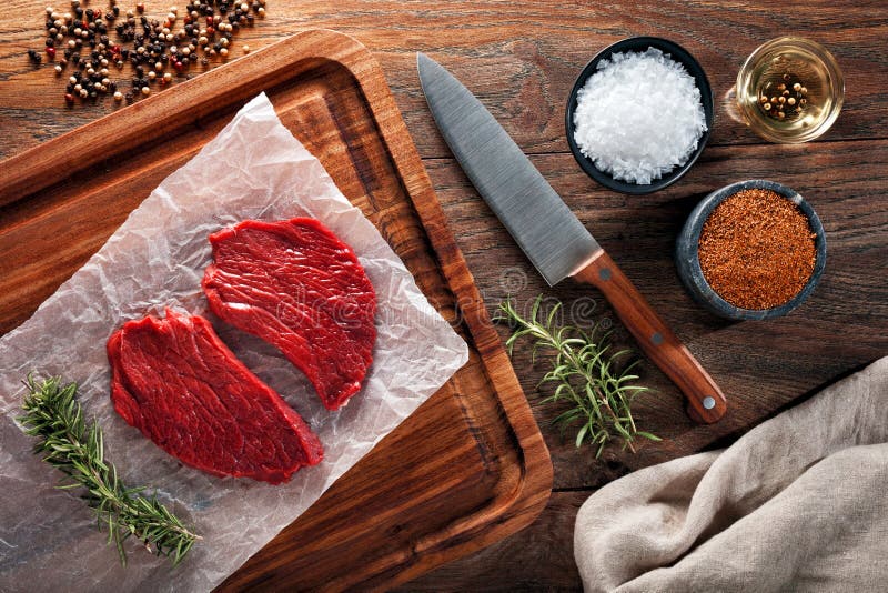 Slices of raw calf beefsteak on white cooking paper and wooden cutting table royalty free stock images Slices of raw calf beefsteak on white cooking paper and wooden cutting table royalty free stock images