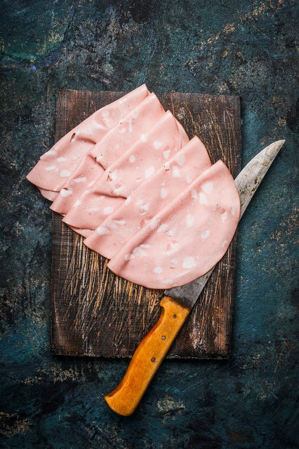 Slices of Sausage Mortadella di Bologna with kitchen knife on rustic wooden background