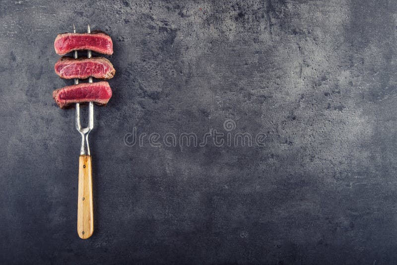 Slices of sirloin beef steak on meat fork on concrete background