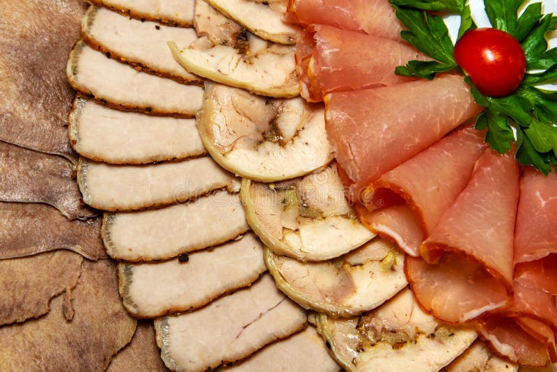 Slicing Different Meats in a Plate with Tomato and Green Leaves on