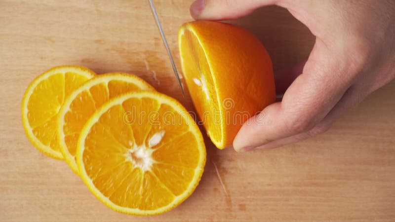 Slicing an orange fruit on a kitchen cutting Board, wooden table as background, close view.