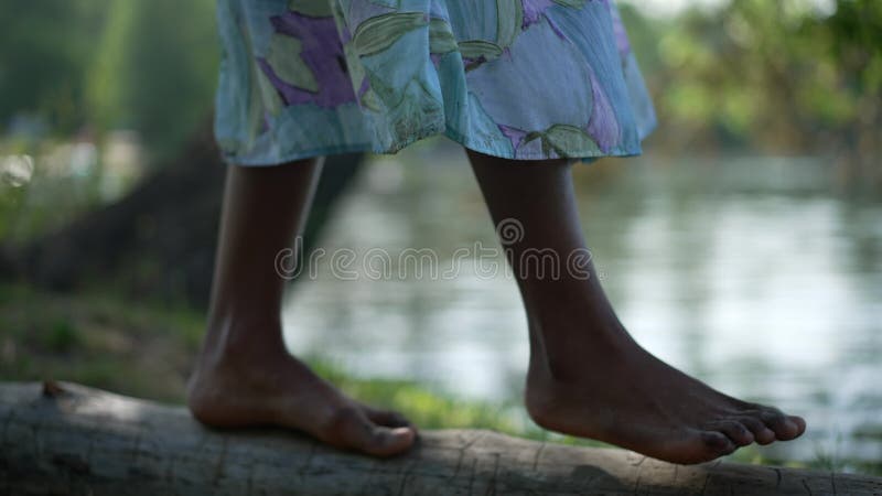 Slim african american femelle pieds marchant sur le tronc d'arbre sur river bank. jeune femme pieds nus méconnaissable en robe