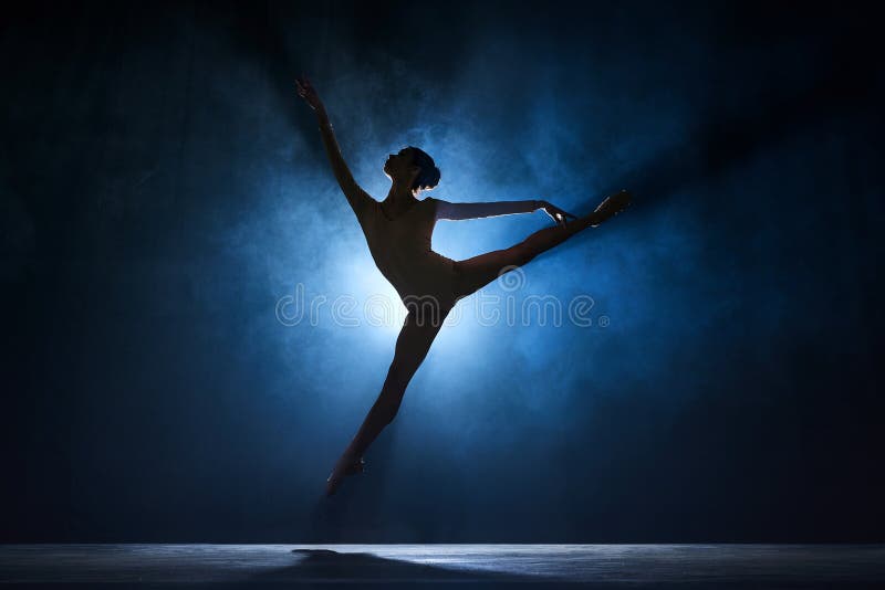 Slim, beautiful, graceful ballerina making creative performance on stage against dark blue background with spotlight