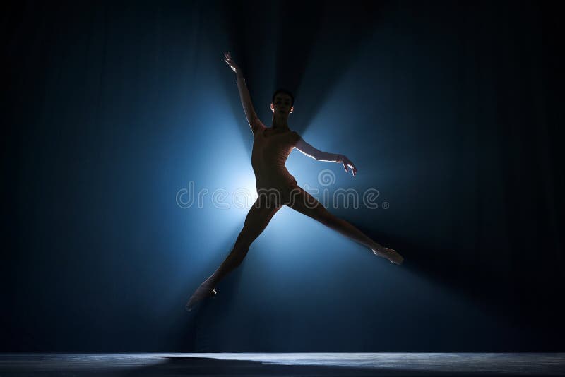 Slim, beautiful, graceful ballerina making creative performance on stage against dark blue background with spotlight