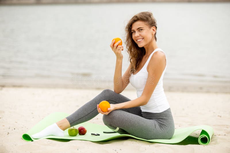 Slim brunet girl holds fruits in her hands siting on a yoga mat on a sandy on a warm windy day stock image Slim brunet girl holds fruits in her hands siting on a yoga mat on a sandy on a warm windy day stock image