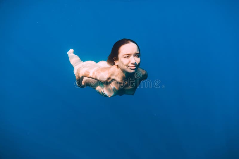 Slim naked woman posing underwater in transparent blue ocean. Nude young women swimming in sea