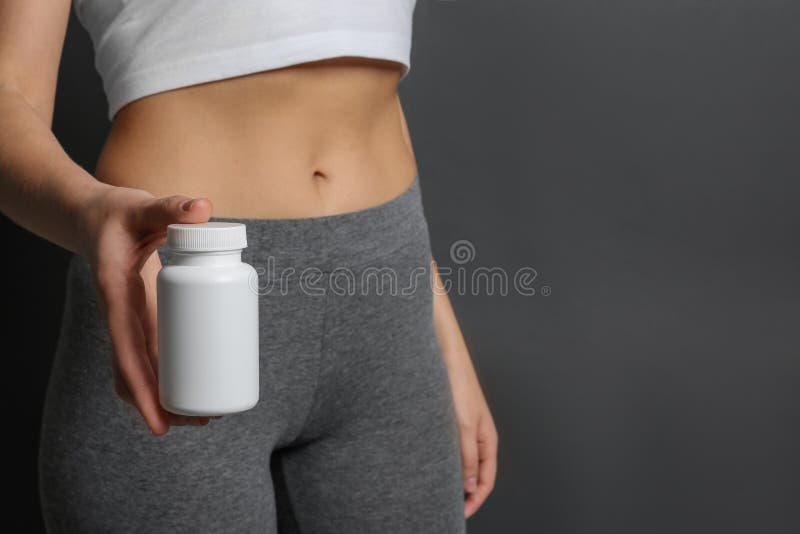 Slim woman holding bottle of weight loss pills against gray background, closeup