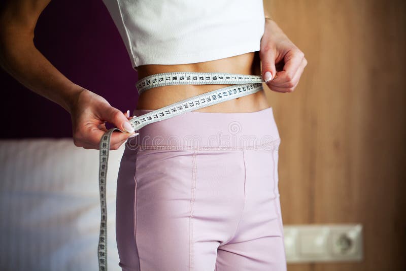 Slim young woman measuring her thin waist with a tape measure