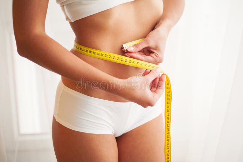 Slender woman measuring her waist with metric tape measure after a
