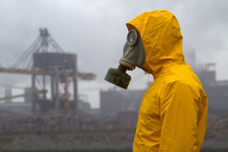 Man wearing gas mask standing infront of factory. Side shot. Background out of focus. Man wearing gas mask standing infront of factory. Side shot. Background out of focus