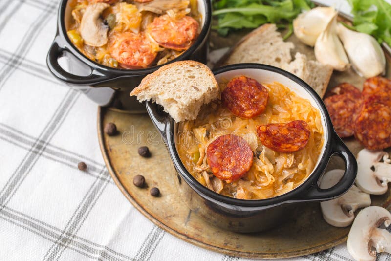 Slovak Christmas national cabbage soup in small black pot with sausage on the tablecloth background