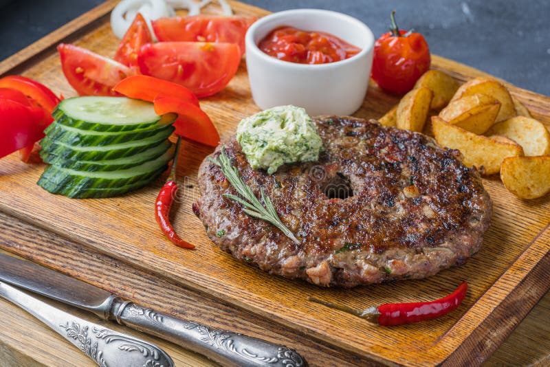 A Slovak meat dishe is on wooden board with tomatoes and fried potatoes