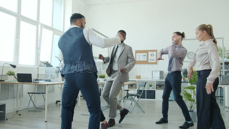 Slow motion di un gruppo multietnico di giovani che ballano divertendo in ufficio