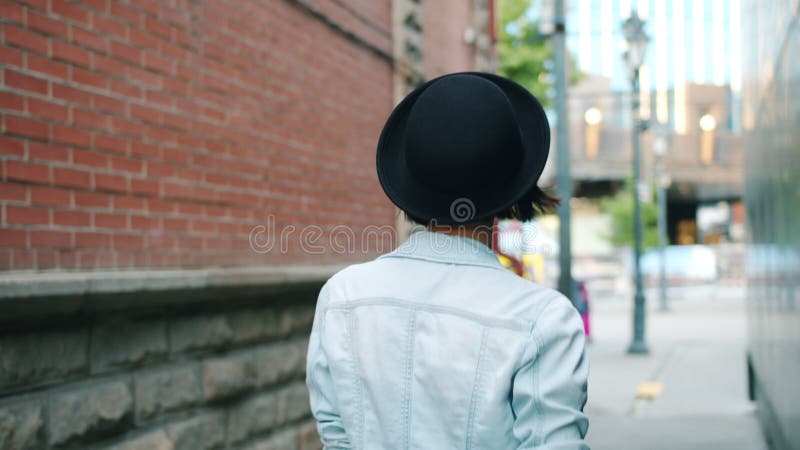 Slow motions of young lady walking outdoors then turning winking touching hat