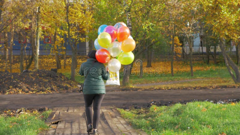 A slowmotion of a woman walking with balloons on a beautiful autumn day