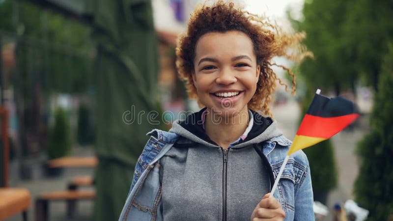 Slowmotion портрет привлекательного Афро-американского туриста в Германии смотря камеру, смеясь над и держа немца