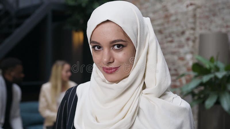 Sluit het portretgezicht van een aantrekkelijke moslimvrouw in de witte hoofddoek van de hijab, kijk naar de camera en glimlach o