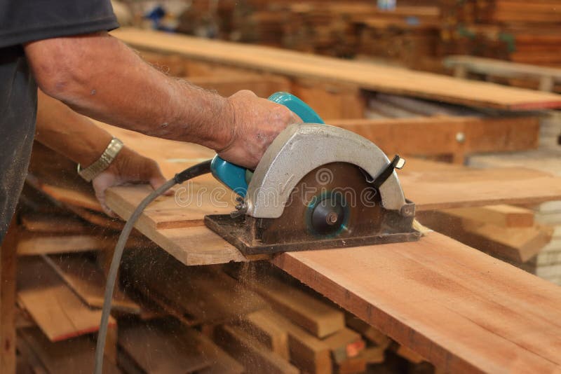 Sluit omhoog handen van hogere timmerman die een stuk van hout snijden tegen elektrische cirkelzaag in timmerwerk woodshop Houtbe stock foto Sluit omhoog handen van hogere timmerman die een stuk van hout snijden tegen elektrische cirkelzaag in timmerwerk woodshop Houtbe stock foto