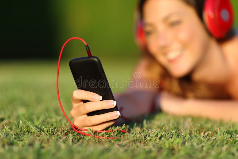 Close up of a woman with headphones holding a smart phone lying on the grass in a park or a garden. Close up of a woman with headphones holding a smart phone lying on the grass in a park or a garden