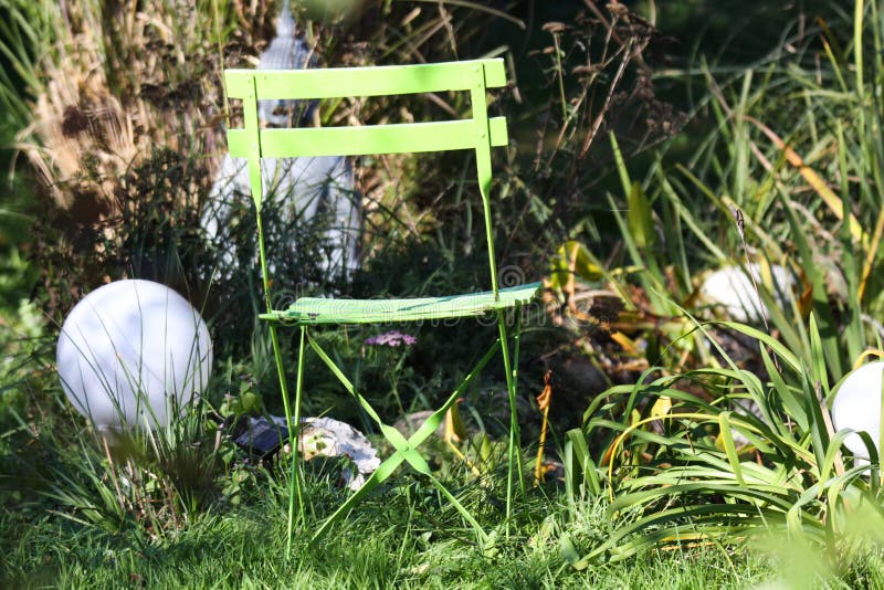 Sluit omhoog van eenzame geïsoleerde groene houten vouwende stoel in de tuin met grassen, groen riet, elektrische ronde lampen royalty-vrije stock foto Sluit omhoog van eenzame geïsoleerde groene houten vouwende stoel in de tuin met grassen, groen riet, elektrische ronde lampen royalty-vrije stock foto
