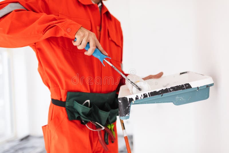 Sluit omhoog voorman in oranje het werkkleren gebruikend het schilderen rolwi stock foto's Sluit omhoog voorman in oranje het werkkleren gebruikend het schilderen rolwi stock foto's
